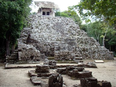 Eine alte Maya-Pyramide aus Stein, umgeben von üppigem Grün und Bäumen, strahlt historische Bedeutung aus.