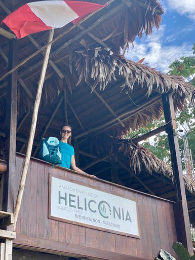 Eine Frau steht auf einem Balkon des Heliconia Amazon River Lodge in Peru, lächelnd mit einem Rucksack auf der Schulter.