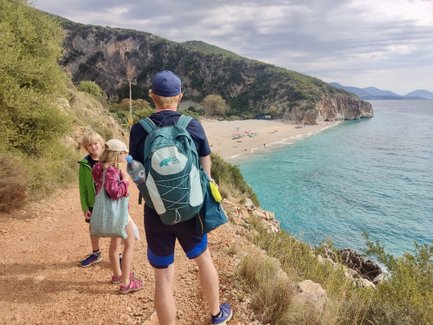 Eine Familie wandert auf einem Pfad mit Blick auf einen schönen Strand und das klare, blaue Wasser des Meeres.