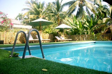 Ein einladender Pool umgeben von üppigem Grün und Palmen, mit Liegen und Sonnenschirmen im Hintergrund.