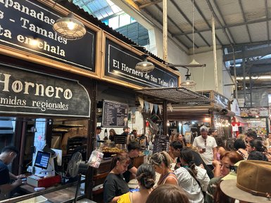 Ein belebter Markt mit vielen Menschen, die an verschiedenen Essensständen in Buenos Aires stehen und regionale Spezialitäten probieren.