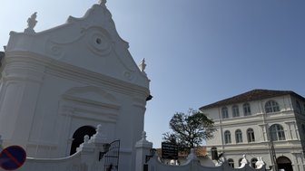 Eine weiße, kunstvoll gestaltete Fassade mit einem großen Tor und einem blauen Himmel im Hintergrund ist zu sehen.