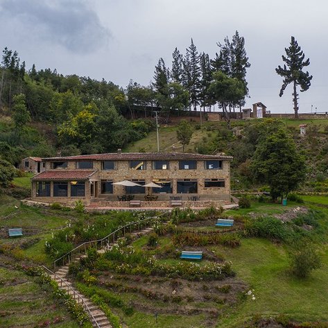 Ein rustikales Steinhaus mit einem begrünten Garten, umgeben von Bäumen und sanften Hügeln, strahlt ländlichen Charme aus.