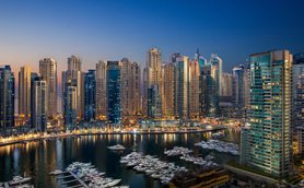 Die Skyline von Dubai bei Dämmerung, mit modernen Wolkenkratzern und einem ruhigen Yachthafen im Vordergrund.