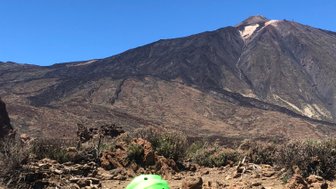 Ein Junge mit einer grünen Kappe sitzt auf dem Boden und betrachtet die Landschaft des Teide-Nationalparks im Hintergrund.
