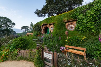 Ein malerisches Hobbit-Haus mit einem begrünten Dach, umgeben von bunten Blumen und einem einladenden Weg.