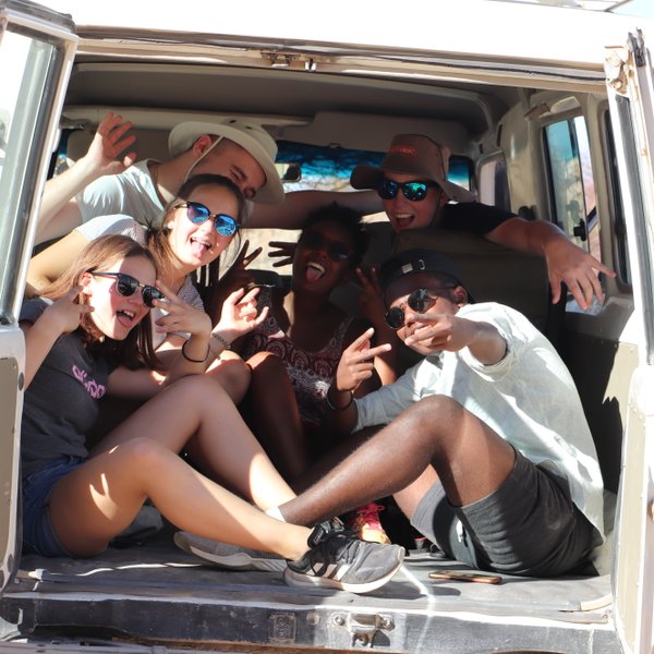 Eine Reisegruppe sitzt gesellig im offenen Kofferraum eines Jeeps - Namibia Urlaub mit Kindern