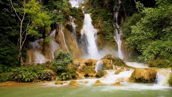 Ein majestätischer Wasserfall stürzt über grüne Felsen, umgeben von üppigem, tropischem Wald und klarem Wasser.
