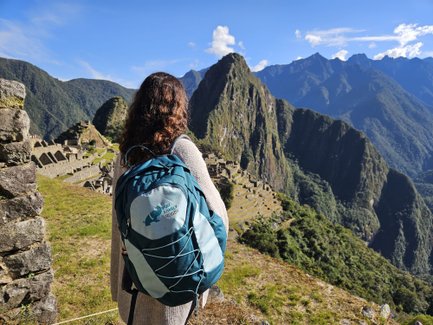 Eine Person mit einem Rucksack steht an einem Aussichtspunkt und blickt auf die beeindruckenden Ruinen von Machu Picchu.