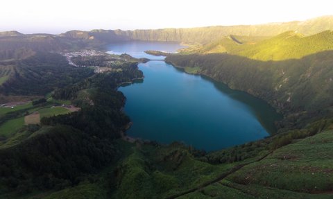 Eine atemberaubende Aussicht auf einen klaren, blauen See, umgeben von üppigen, grünen Hügeln und Bergen im Hintergrund.