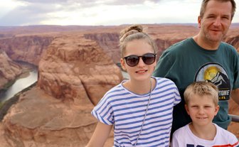 Eine Familie steht am Rand des Horseshoe Bend, umgeben von beeindruckenden roten Felsen und einem Fluss im Hintergrund.