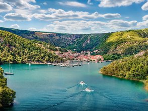 Eine malerische Küstenstadt in Kroatien, umgeben von grünen Hügeln und klarem Wasser, mit Segelbooten im Hafen.