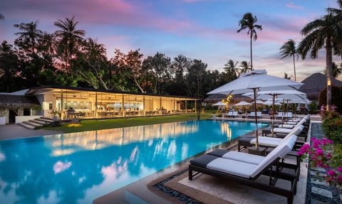 Ein luxuriöser Pool mit Liegen und Sonnenschirmen, umgeben von üppigem Grün und einem atemberaubenden Sonnenuntergang.