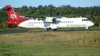 Ein Flugzeug von Air Madagascar steht auf einer Landebahn, umgeben von üppigem Grün und klarem Himmel.