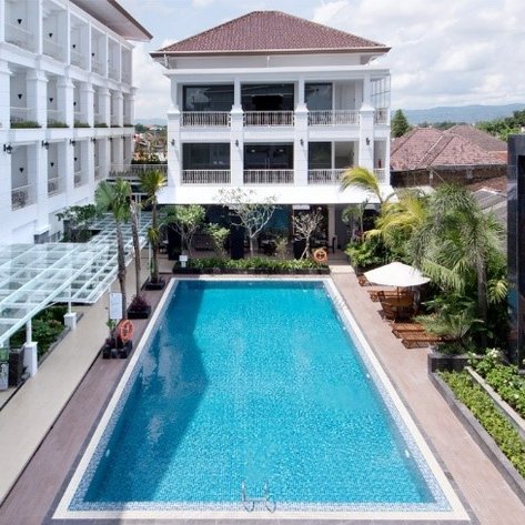 Ein klarer Pool spiegelt den Himmel wider, umgeben von modernen Gebäuden und üppigem Grün, ideal für Entspannung.