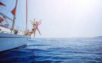 Drei Kinder springen fröhlich von einer Yacht ins glitzernde blaue Wasser, umgeben von einem klaren Himmel.