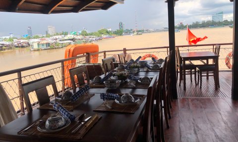 Ein gemütlicher Tisch auf einem Boot, gedeckt mit traditionellem Geschirr, bietet einen Blick auf den Fluss und die Stadt im Hintergrund.
