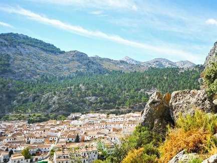 Zwei Wanderer stehen auf einem Aussichtspunkt und blicken auf das malerische Dorf Grazalema, umgeben von Bergen und Wäldern.