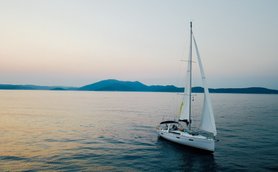 Ein Segelboot gleitet sanft über das ruhige Wasser, umgeben von sanften Hügeln im Hintergrund und einem zarten Abendhimmel.
