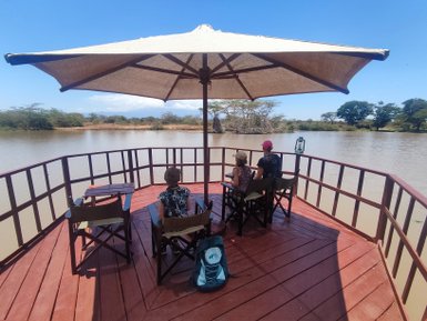 Drei Personen sitzen entspannt auf einer Holzterrasse, die über einen ruhigen See mit grünen Ufern blickt.