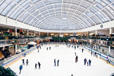 Eine belebte Eislaufbahn im West Edmonton Mall, umgeben von Geschäften und fröhlichen Besuchern, die Spaß haben.