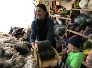 Eine fröhliche Frau und ein Junge arbeiten gemeinsam an einem Wollprojekt in einem hellen, gemütlichen Raum voller Materialien.