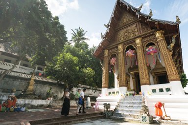 Ein prächtiger buddhistischer Tempel mit kunstvollen Verzierungen und bunten Laternen, umgeben von üppigem Grün.