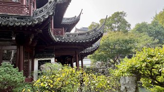 Ein traditionelles chinesisches Gebäude mit geschwungenem Dach, umgeben von üppigem Grün und einem ruhigen Teich.