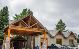 Die Außenansicht eines Resorts mit einem großen Holzvordach und modernen Fenstern, umgeben von Bäumen und Autos.