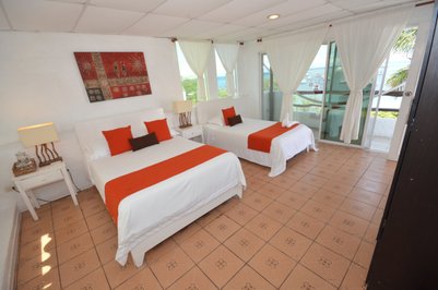 Ein helles Zimmer mit zwei Betten, orangefarbenen Akzenten und Blick auf das Meer durch große Fenster.