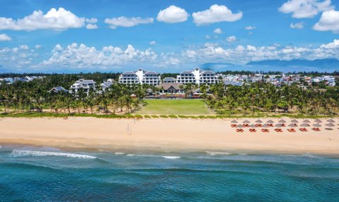 Ein atemberaubender Blick auf den Hoi An Strand mit einem luxuriösen Resort im Hintergrund und Palmen, die sanft im Wind wiegen.