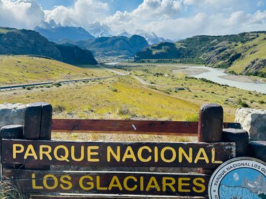 Ein Holzschild mit der Aufschrift 'Parque Nacional Los Glaciares' steht vor einer beeindruckenden Berglandschaft.