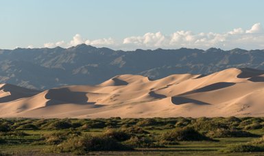 Sanfte Sanddünen erstrecken sich über die Landschaft, während die Berge im Hintergrund in sanften Schatten liegen.