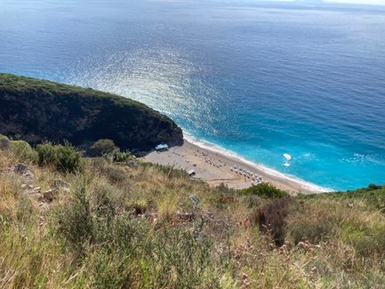 Ein atemberaubender Blick auf den Gjipe Strand, umgeben von grünen Hügeln und glitzerndem, blauem Wasser.