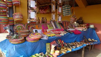 Bunte handgefertigte Körbe und Kunsthandwerk sind auf einem blauen Tuch in einem Marktstand ausgestellt.