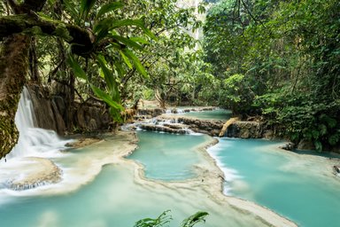Ein ruhiger Wasserfall fließt sanft in einen türkisfarbenen Pool, umgeben von üppigem, grünem Dschungel.