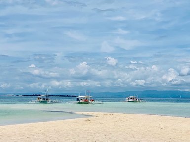 Drei traditionelle philippinische Auslegerboote gleiten sanft über das klare Wasser, umgeben von einem strahlend blauen Himmel.