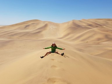 Ein Kind sitzt auf den Kamm einer Düne in der Wüste - Namibia Urlaub mit Kindern