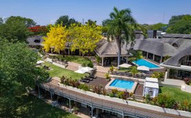 Eine weitläufige Hotelanlage mit einem Pool, umgeben von üppigem Grün und bunten Blumen, strahlt tropisches Flair aus.