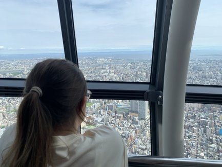 Eine Person mit einem Pferdeschwanz blickt aus dem Fenster des Tokio Skytree auf die weitläufige Stadtlandschaft.