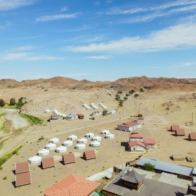 Eine weite Landschaft mit Jurten und kleinen Häusern, umgeben von sanften Hügeln und einem klaren blauen Himmel.