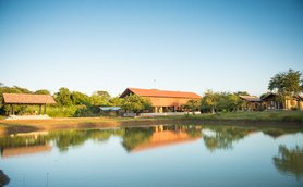 Ein ruhiger Blick auf eine Villa in Sri Lanka, umgeben von üppigem Grün und einem glitzernden Teich im Vordergrund.