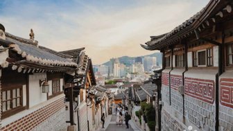 Eine malerische Straße in Bukchon Hanok Village, gesäumt von traditionellen koreanischen Häusern und modernen Gebäuden im Hintergrund.