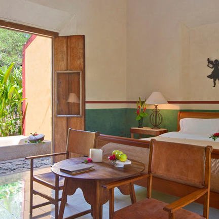 Ein helles Hotelzimmer mit einem großen Bett, einem Tisch und Stühlen, das durch offene Türen mit Blick auf einen Garten erhellt wird.