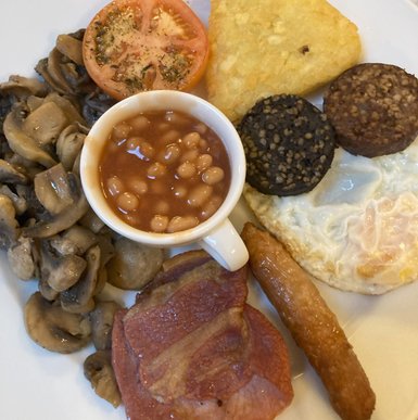 Ein traditionelles irisches Frühstück mit gebratenem Speck, Würstchen, Eiern und gebackenen Bohnen auf einem weißen Teller.