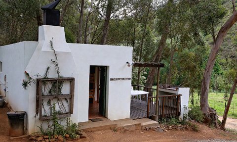 Ein charmantes, weißes Cottage mit einem Holzdeck, umgeben von üppigem Grün und Eukalyptusbäumen, strahlt Ruhe aus.