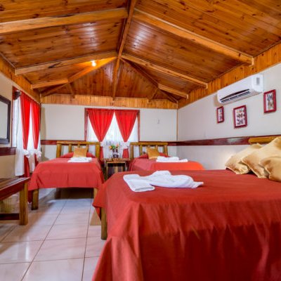 Ein gemütliches Zimmer mit Holzwänden, roten Vorhängen und drei Betten, die mit weißen Handtüchern dekoriert sind.