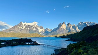 Majestätische Berge mit schneebedeckten Gipfeln erheben sich über einen ruhigen blauen See, umgeben von üppigem Grün.
