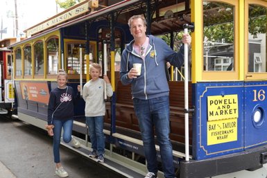 Eine Familie steht an einer Straßenbahn in San Francisco, lächelnd und bereit für ein Abenteuer in der Stadt.