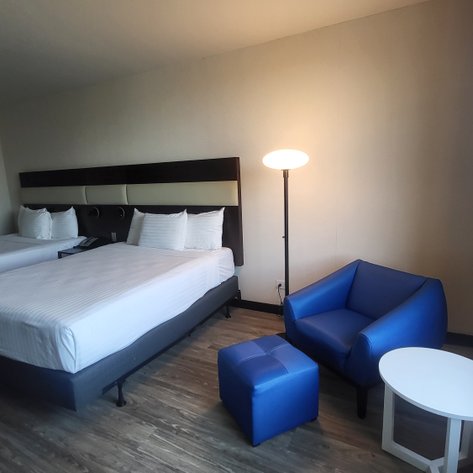 Ein modernes Hotelzimmer mit zwei Einzelbetten, einem blauen Sessel und einem kleinen Tisch, ideal für Entspannung.